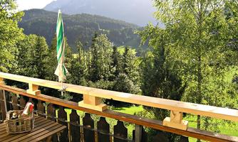 A picturesque balcony overlooking green forests and mountains. The table and the sun umbrella invite you to relax.