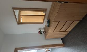 A bright hallway with a wooden wardrobe and a mirror. On the wardrobe, there is a small flower vase and a towel.