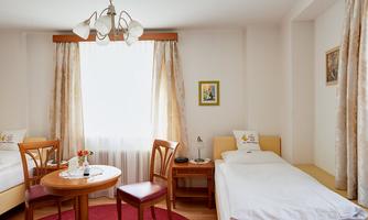 A bright room with two beds and a small table.  
Large windows let in a lot of light and the floor is covered with a red carpet.