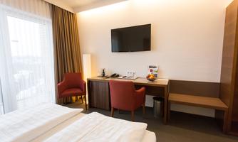 A modern hotel room with two beds, a television, and a desk. There is a small table with fruit and two comfortable chairs.