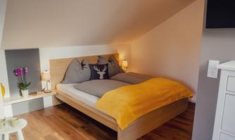 A cozy bedroom with a wooden bed and soft pillows. The warm colors and soft light create an inviting atmosphere.