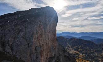 A majestic rock formation under a cloudy sky. The sun shines over the mountains and the autumn landscape.