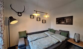 A cozy living room with a couch and modern lamps. Pictures and a deer antler hang on the wall, adding a rustic touch to the space.