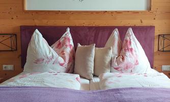 A cozy bedroom with a large bed, surrounded by wood paneling. A saying hangs on the wall, inviting happiness.