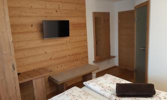 A simple room with wooden walls, a television, and two beds. There is a table and a mirror on the wall.