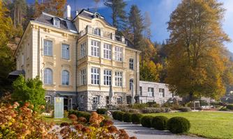 An elegant, historic building surrounded by colorful autumn leaves. The garden is well-maintained and invites you to linger.
