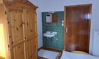 A simple room with a wooden wardrobe, a sink, and a wooden door. The room has green tiles and a white carpet.