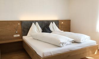 A cozy bedroom with a large wooden bed and white bedcovers. The walls are light, and the room feels inviting and modern.