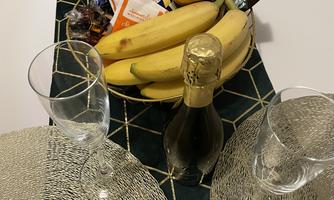 A beautifully set table with two glasses and a bottle of sparkling wine. On the tablecloth, there are fruits and snacks.