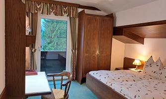 A cozy bedroom with a double bed and a desk. The windows offer a view of trees and let in plenty of natural light.