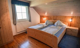 A cozy bedroom with a large wooden bed and two pillows. The walls are made of wood, and there is a window with curtains.
