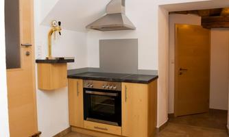 A modern kitchen with wooden fronts and an oven. The wall is bright and the floor is tiled.