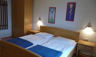 A cozy bedroom with a wooden bed and two nightstands. Colorful pictures hang on the walls, and there is a wooden dresser.