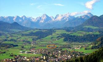 A picturesque landscape with green fields and small villages. In the background, majestic mountains rise under a clear sky.