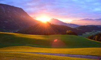 A picturesque sunset over green hills and mountains. The gentle rays of light illuminate the landscape.