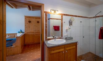 A modern bathroom with wooden cabinets and a sink. There is a shower and an area with tiles and carpet.