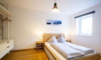 A cozy bedroom with a double bed and modern accents. There is a large window with natural light and a minimalist decor.