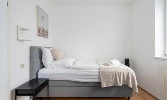A simple bedroom with a single bed and soft pillows. The walls are bright, and the decor is minimalist.