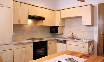 A modern kitchen with light wood cabinets and a black stove. Some magazines and a tablecloth are on the table.