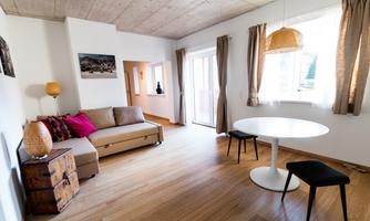 A bright living room with a sofa and a round table. Large windows provide plenty of daylight.