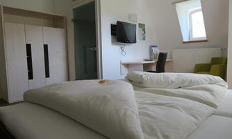 A spacious room with a double bed and a desk. In the background, there is a television and a wardrobe.