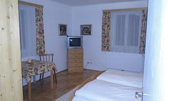A simple room with two single beds and a table. There is a television and decorative window curtains.