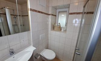 A modern bathroom with tiles and bright lighting. There is a sink, a shower, and a windowsill with a basket.