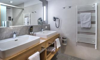 A modern bathroom with a double sink and wooden shelf. The walls are bright, and the space feels inviting and clean.