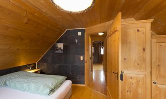 A cozy bedroom with wood paneling and a double bed. The rooms are bright and simply decorated, with access to another room.