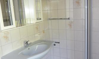 A simple bathroom with a shower and a sink. The walls are covered with white tiles.
