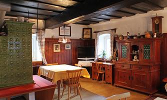 A cozy dining room with wooden furniture and rustic charm. The green tiled stove and the soft colors create an inviting atmosphere.
