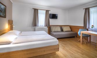 A cozy room with a double bed and a seating area. Natural light sources and wooden paneling create an inviting atmosphere.