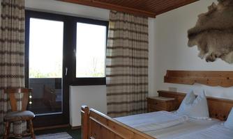 A cozy bedroom with wooden furniture and a balcony. Large windows let in plenty of light and offer a view outside.