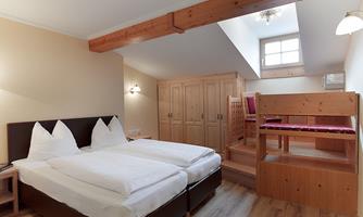A cozy bedroom with two single beds and wooden details. The room has a small workspace and a built-in wardrobe.