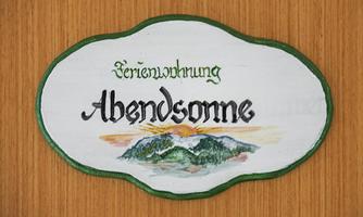 A sign with the inscription “Holiday Apartment Evening Sun”. Below is a picturesque view of mountains and a sunset.