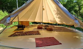 A cozy tent with a carpeted floor and some furniture. Green trees surround the campsite, creating a relaxed atmosphere.