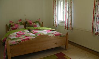A cozy bedroom with a double bed and colorful bedding. Bright walls and a large window create a friendly atmosphere.