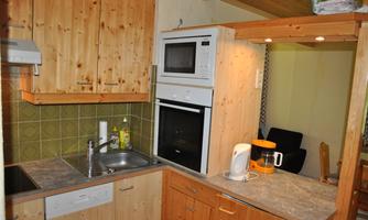 A modern kitchen with wooden cabinets and a stone countertop. It features basic appliances such as a stove, a microwave, and a kettle.