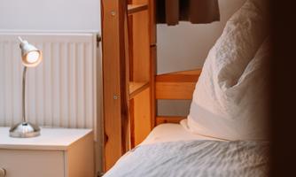A cozy bedroom with a bunk bed. A table lamp is on the table and the bed linen is neatly folded.