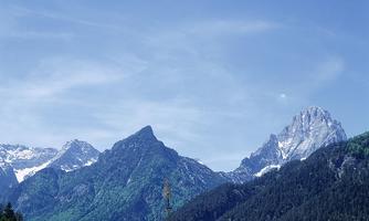 An impressive mountain landscape with snow-capped peaks and lush greenery. The clear blue sky complements the picturesque panorama.