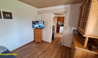 A living room with a television and a wooden cabinet. The walls are white and the floor is made of laminate.