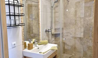 A modern bathroom with a large glass shower and elegant tiles. The vanity has a wood finish and is decorated with towels.
