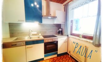 A modern kitchen with blue and white cabinets. It is well-equipped with a stove, sink, and a window that lets in plenty of light.