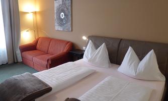 A cozy hotel room with a large bed and two pillows. In the background, there is a red sofa and a piece of art on the wall.