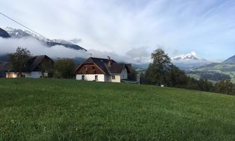 A picturesque landscape with traditional houses and green meadows. In the background, majestic mountains rise under a cloudy sky.