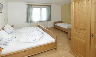 A bright bedroom with two wooden beds and large windows. The room is cozy and simply furnished.
