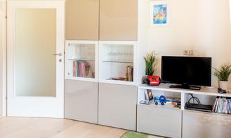 A modern living space with a television and a bookshelf. The room feels bright and inviting with a clear glass door.