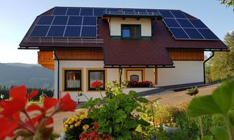 A modern house with solar panels on the roof.  
Surrounded by colorful flowers and beautiful scenery.