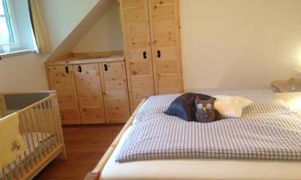 A cozy bedroom with a large bed and a children's bed. Wooden cabinets and bright light create a warm atmosphere.