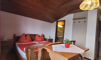 A cozy room view with a double bed and a small table. The walls are made of wood and decorated, and there is a plant pot on the table.